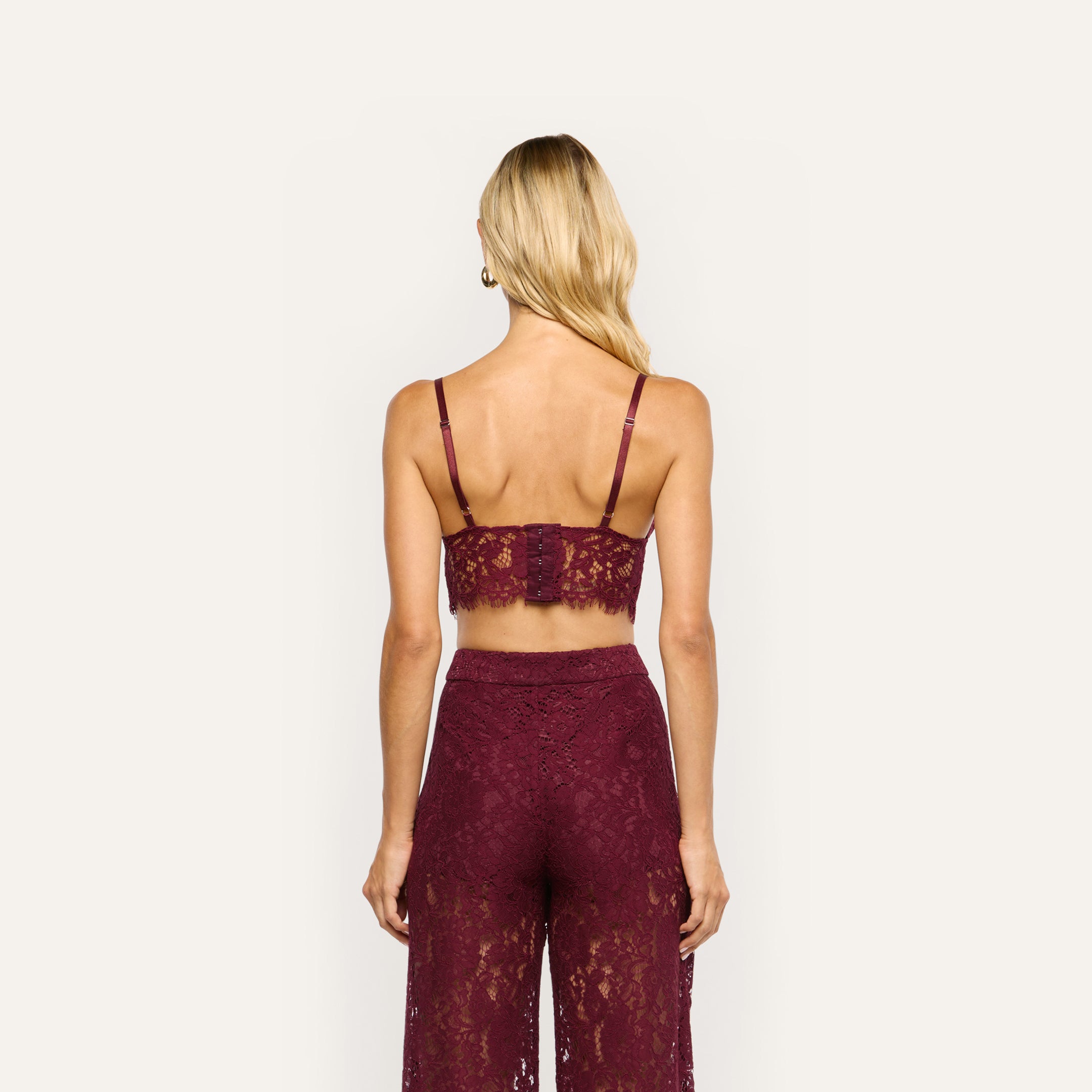 A person seen from behind wearing an Aislin Lace Bralette and matching trousers in burgundy sheer stretch lace with scalloped edges.