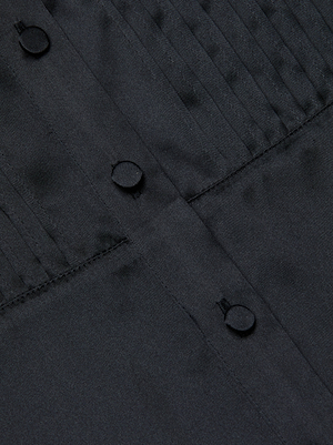 Close-up of the Divya Silk Shirt by L'AGENCE, showcasing black silk fabric with pleated detailing and satin-covered buttons along a vertical seam.