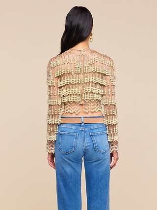 Wearing the Rogan Pearl Fringe Top with blue jeans, a person with long dark hair stands facing away from the camera against a beige background—a look evoking NYFW Fall 2026 trends.