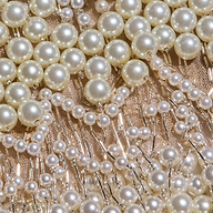 Close-up of rows of white pearls and small beads sewn onto a light, sheer mesh fabric with metallic threads, creating an intricate, decorative pattern reminiscent of the Rogan Pearl Fringe Top.