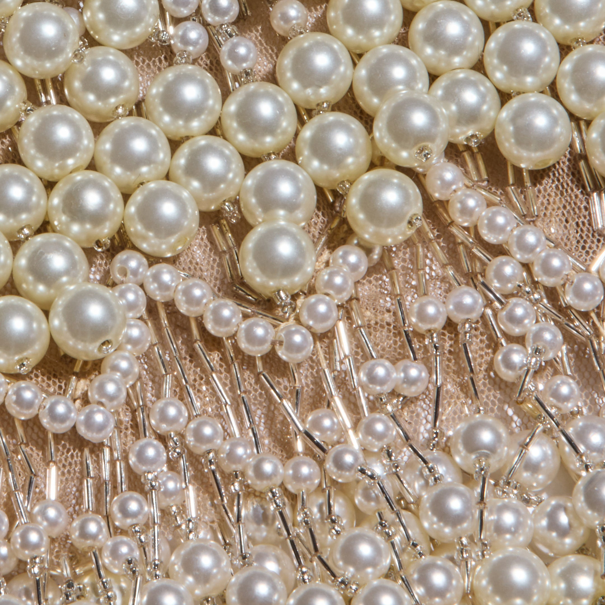 Close-up of rows of white pearls and small beads sewn onto a light, sheer mesh fabric with metallic threads, creating an intricate, decorative pattern reminiscent of the Rogan Pearl Fringe Top.