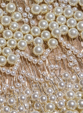 Close-up of various sizes of white pearls sewn onto beige mesh fabric, forming a decorative and textured pattern with intricate beadwork details—an elegant touch inspired by the Rogan Pearl Fringe Top as seen on the NYFW Fall 2026 runways.