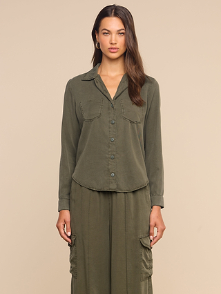 A woman wearing the Isla Shirt in olive green, crafted from featherweight twill with chest pockets, paired with matching cargo pants, stands against a plain beige background and looks at the camera with a neutral expression.