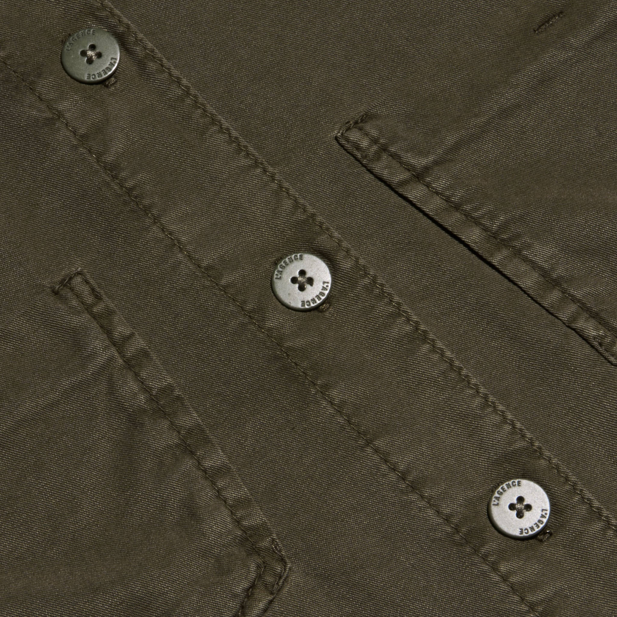 Close-up of the Isla Shirt in olive green featherweight twill, featuring two flap pockets and three four-hole metallic buttons engraved with small text around their edges.