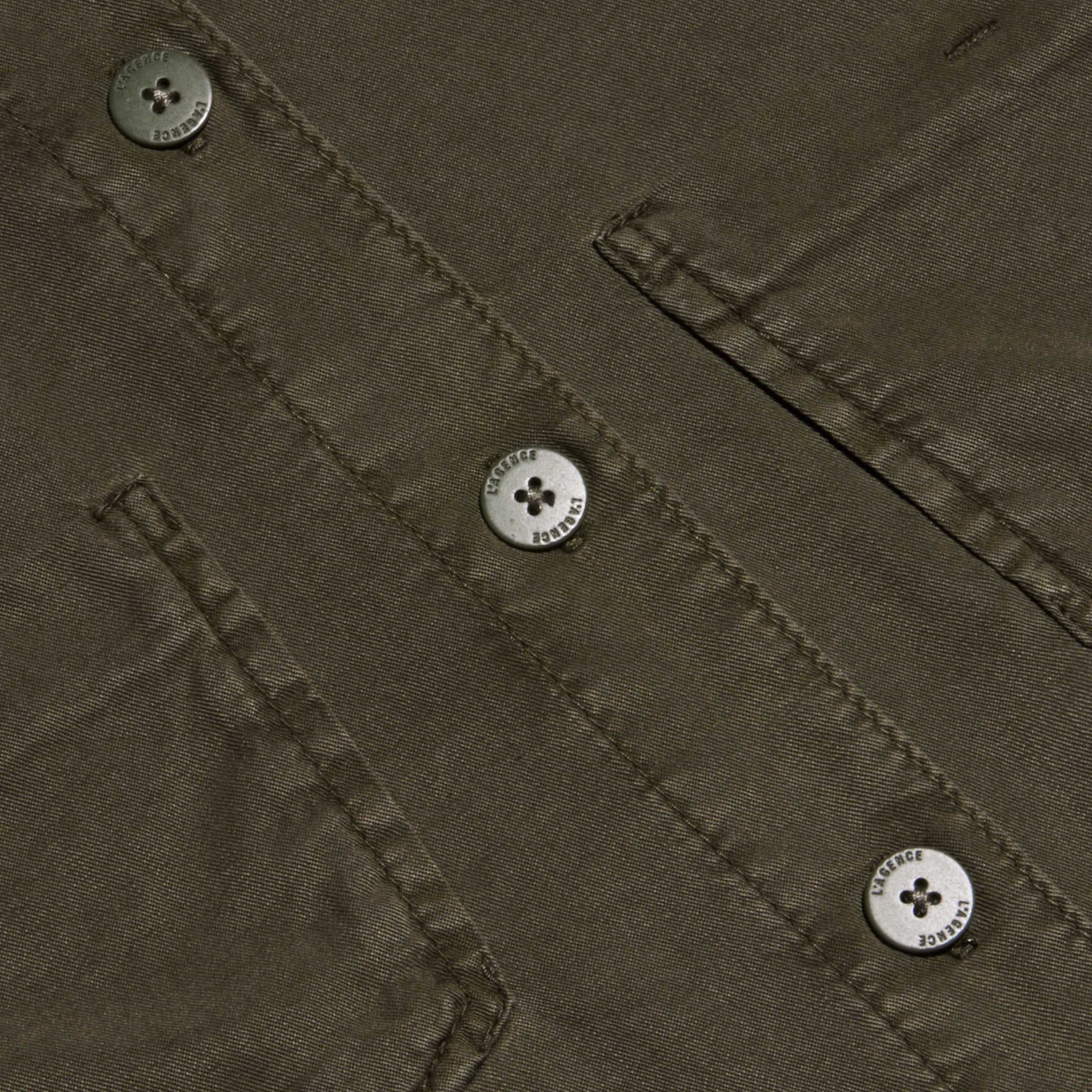 Close-up of the Isla Shirt in olive green featherweight twill, featuring two flap pockets and three four-hole metallic buttons engraved with small text around their edges.