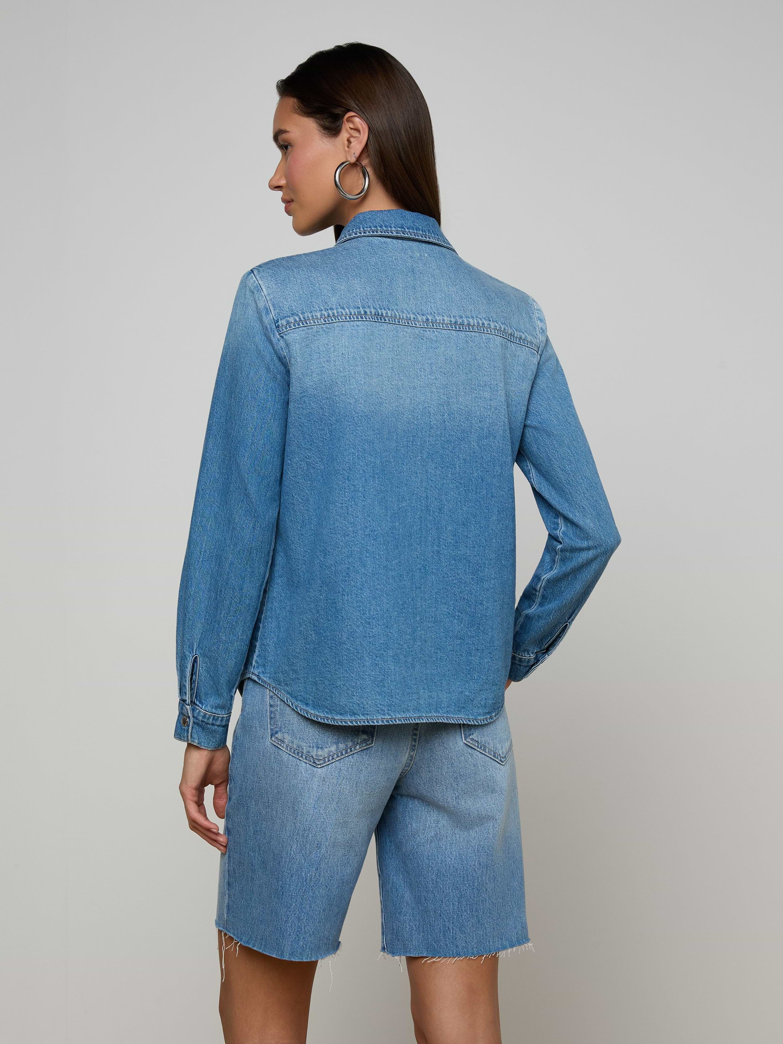 A woman stands with her back to the camera, wearing the lightweight Isla Shirt and matching denim shorts in an aged indigo wash, set against a plain off-white background.