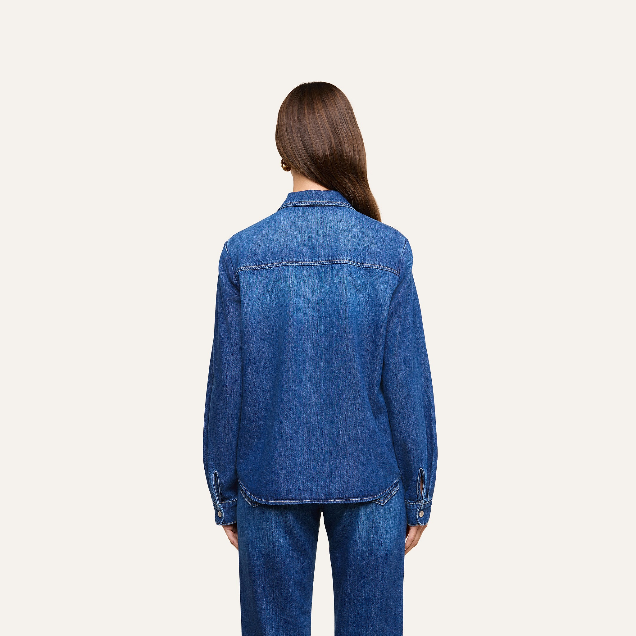 A person with long brown hair is facing away, wearing the lightweight Isla Shirt and jeans against a plain, light background.