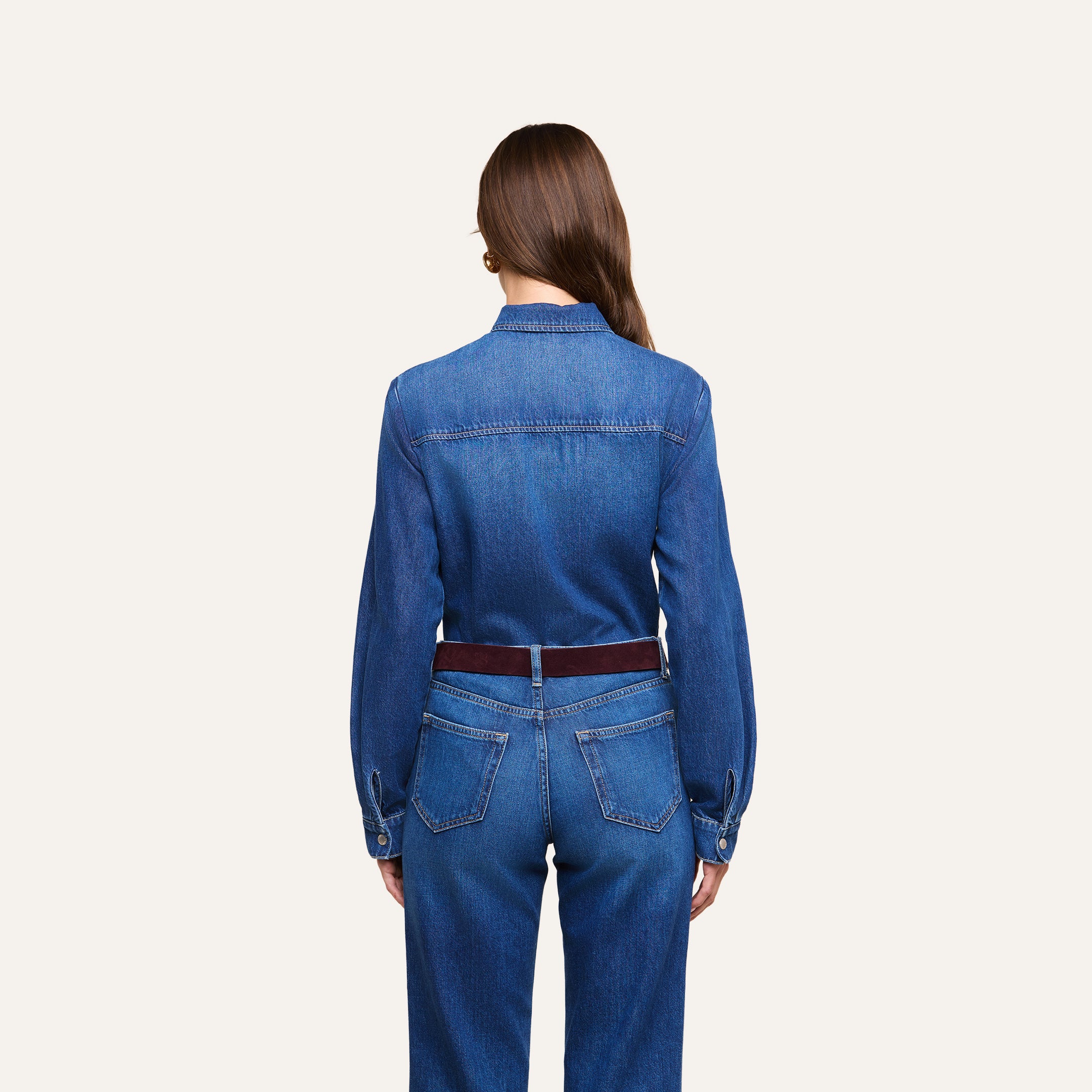 A woman with long brown hair, wearing the Isla Shirt and jeans, is standing with her back to the camera against a plain light background.