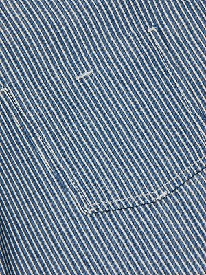 Close-up of the Isla Shirt by L’AGENCE, a featherweight denim top in indigo pinstripe with visible stitching and a pocket on diagonally striped fabric.