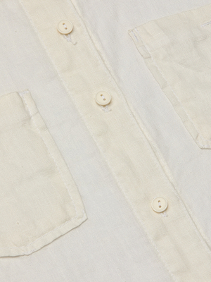 Close-up of the Isla Linen Shirt in ecru, featuring three white buttons on the placket and part of the left chest pocket. The image highlights the textured linen fabric and fine stitching details of this classic button-down design.