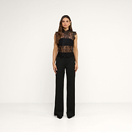 A woman with long brown hair and a neutral expression stands facing forward in a minimal studio, wearing the Tours Lace Top and black wide-leg pants. The background is plain white.