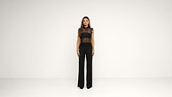 A woman stands facing forward in a plain white room, wearing a black sleeveless lace top and black wide-leg pants. The background is empty and minimalistic.