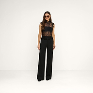 A woman wearing sunglasses, the Tours Lace Top, and high-waisted black pants stands against a plain white background.