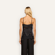 A woman with long blonde hair, seen from behind against a plain light background, wears the Mitsu Satin Lace Camisole paired with matching wide-leg black pants. The camisole features lingerie-inspired styling with delicate lace detailing.