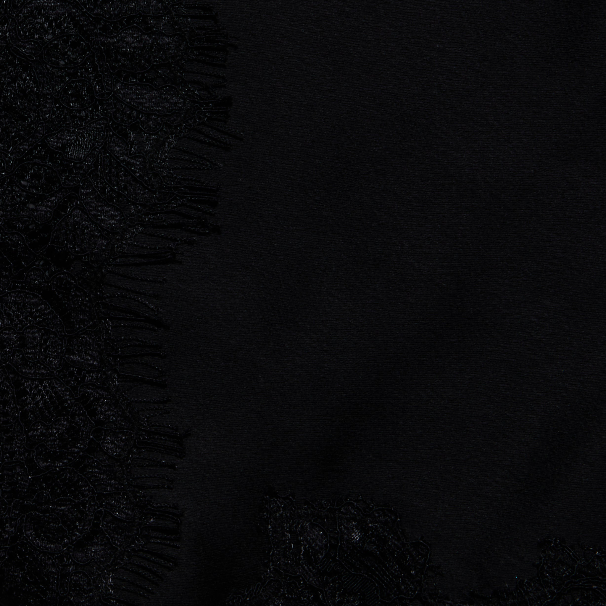 Close-up of black fabric with a lace pattern and fringed edges on the left side, contrasting with smooth, plain black satin to the right—evoking the elegant detailing of the Mitsu Satin Lace Camisole.