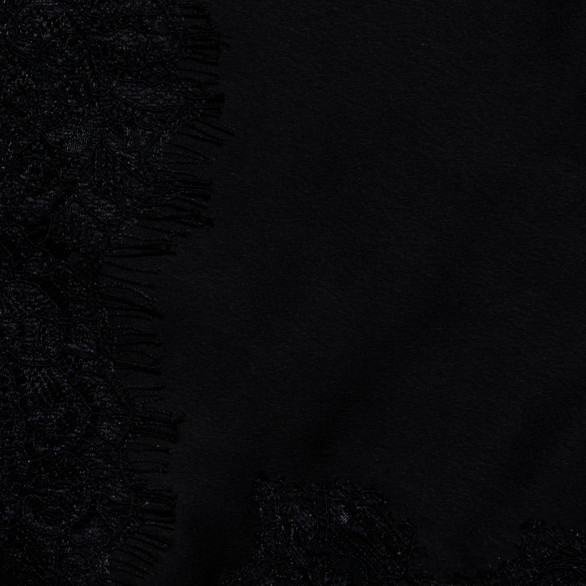 Close-up of black fabric with a lace pattern and fringed edges on the left side, contrasting with smooth, plain black satin to the right—evoking the elegant detailing of the Mitsu Satin Lace Camisole.