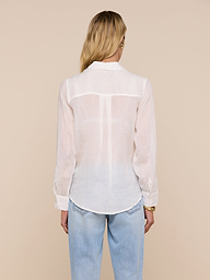 A person with long blonde hair, wearing the Ellery Blouse and light blue jeans, is standing with their back to the camera against a plain light background.