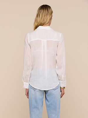 A person with long blonde hair, wearing the Ellery Blouse and light blue jeans, stands facing away from the camera against a beige background.