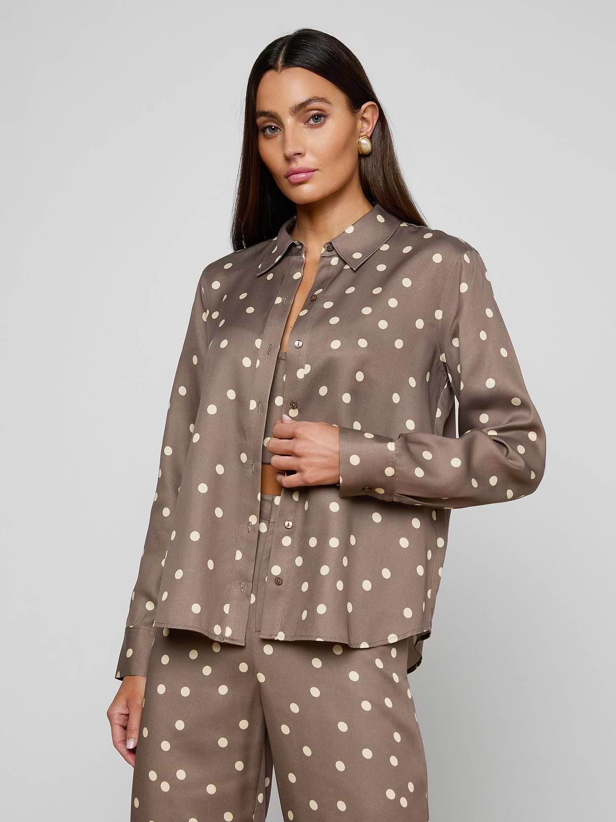 A woman wearing the Ellery Button-Down Shirt in cardamom brown with white polka dots and matching pants, standing against a plain light background.