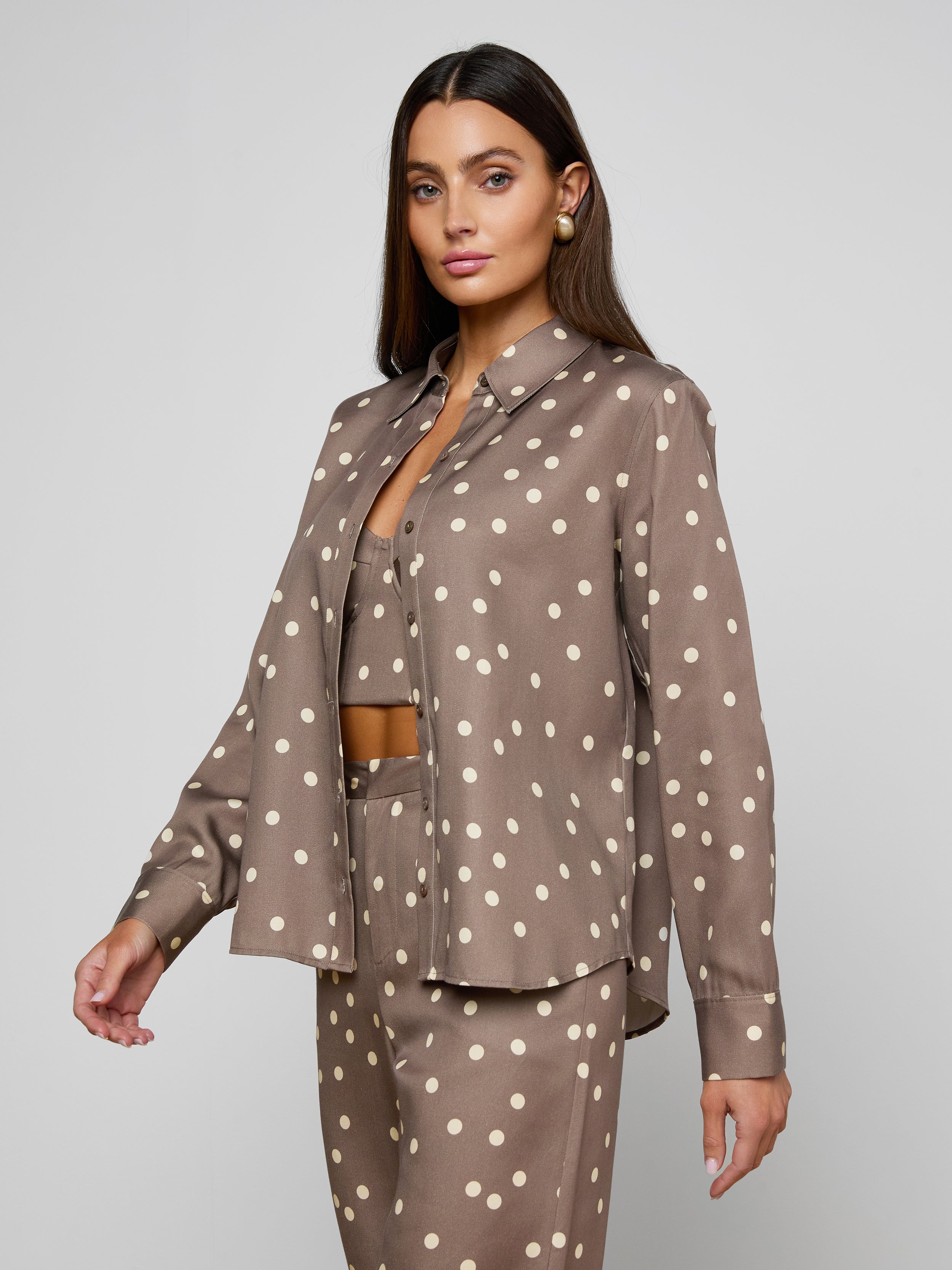 Woman wearing the Ellery Button-Down Shirt in cardamom brown with white polka dots, paired with matching long-sleeve pants and a coordinating crop top, standing against a plain light background.