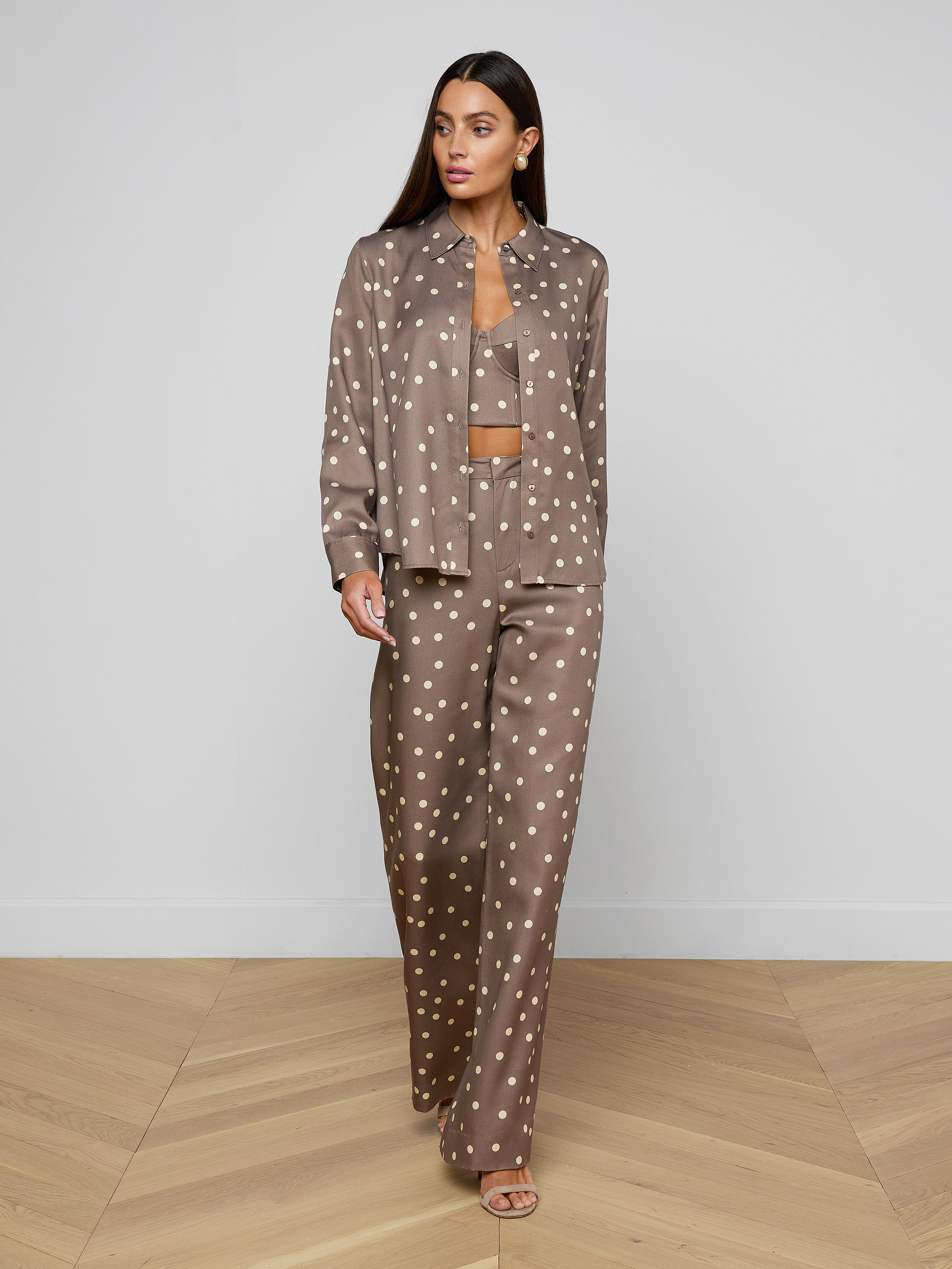 Wearing the Ellery Button-Down Shirt in taupe polka-dot, paired with a cropped tank and matching pants, a person stands against a plain white background.
