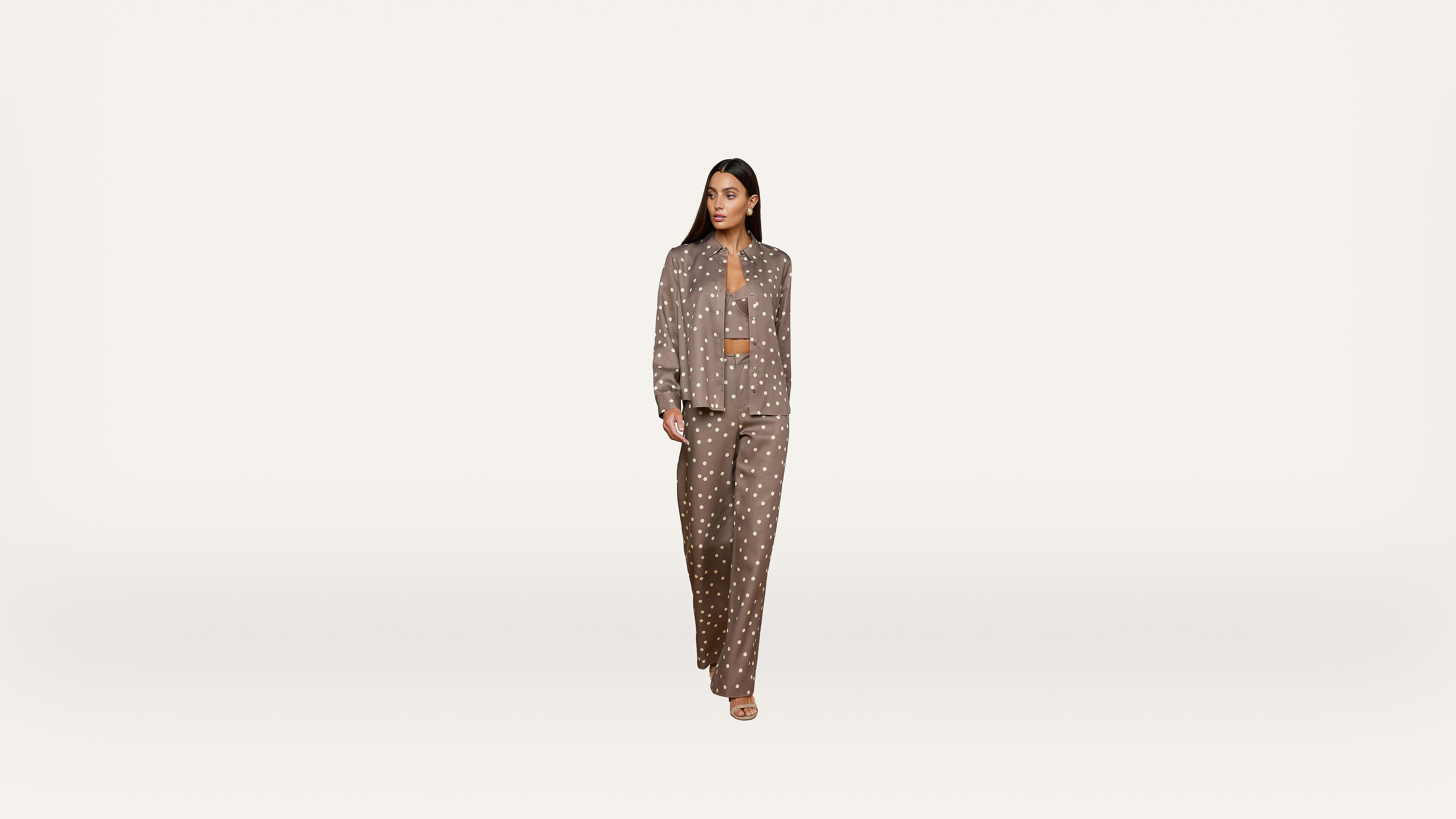 Woman wearing a brown pajama-style pantsuit with white polka dots, walking forward against a plain white background.