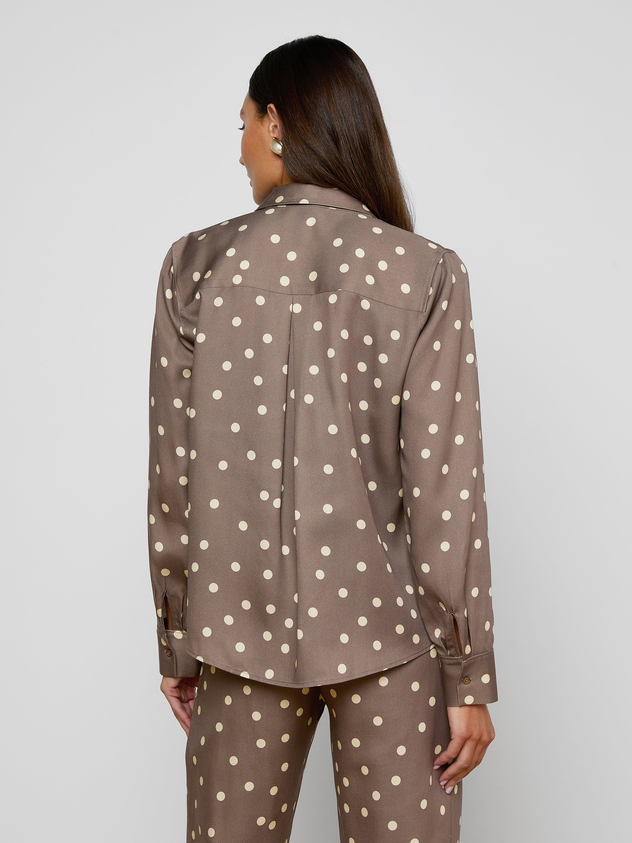 A person with long brown hair is facing away, wearing the Ellery Button-Down Shirt in cardamom brown with matching white polka dot pants, set against a plain light background.
