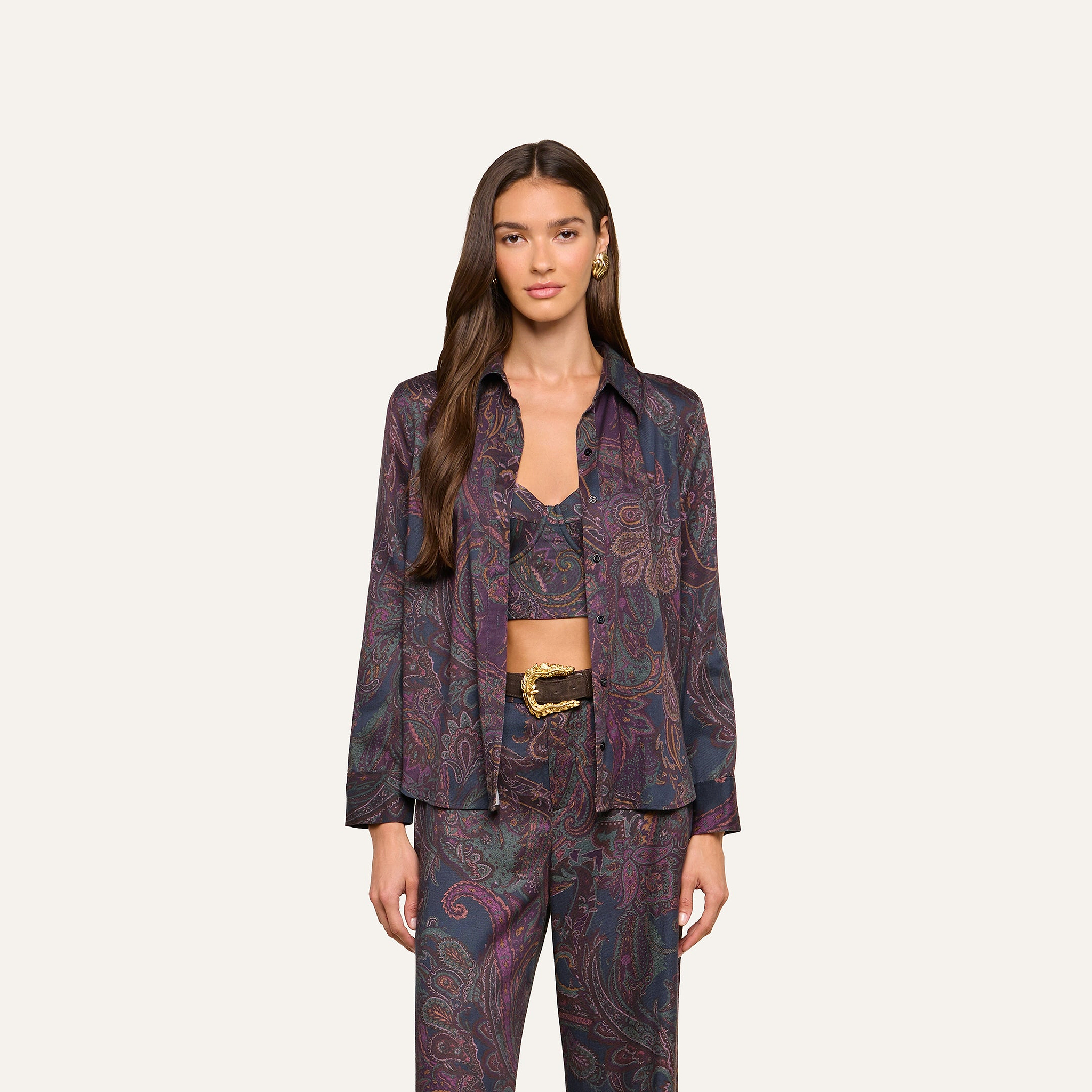 A woman wearing the Ellery Button-Down Shirt as part of a coordinated lightweight twill set with a paisley print blouse, crop top, and pants, stands against a plain light background, looking at the camera with a neutral expression.