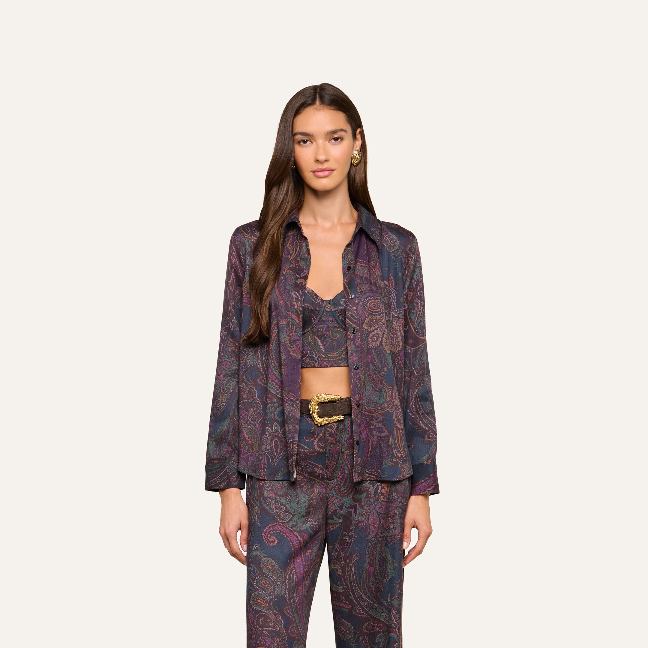 A woman wearing the Ellery Button-Down Shirt as part of a coordinated lightweight twill set with a paisley print blouse, crop top, and pants, stands against a plain light background, looking at the camera with a neutral expression.
