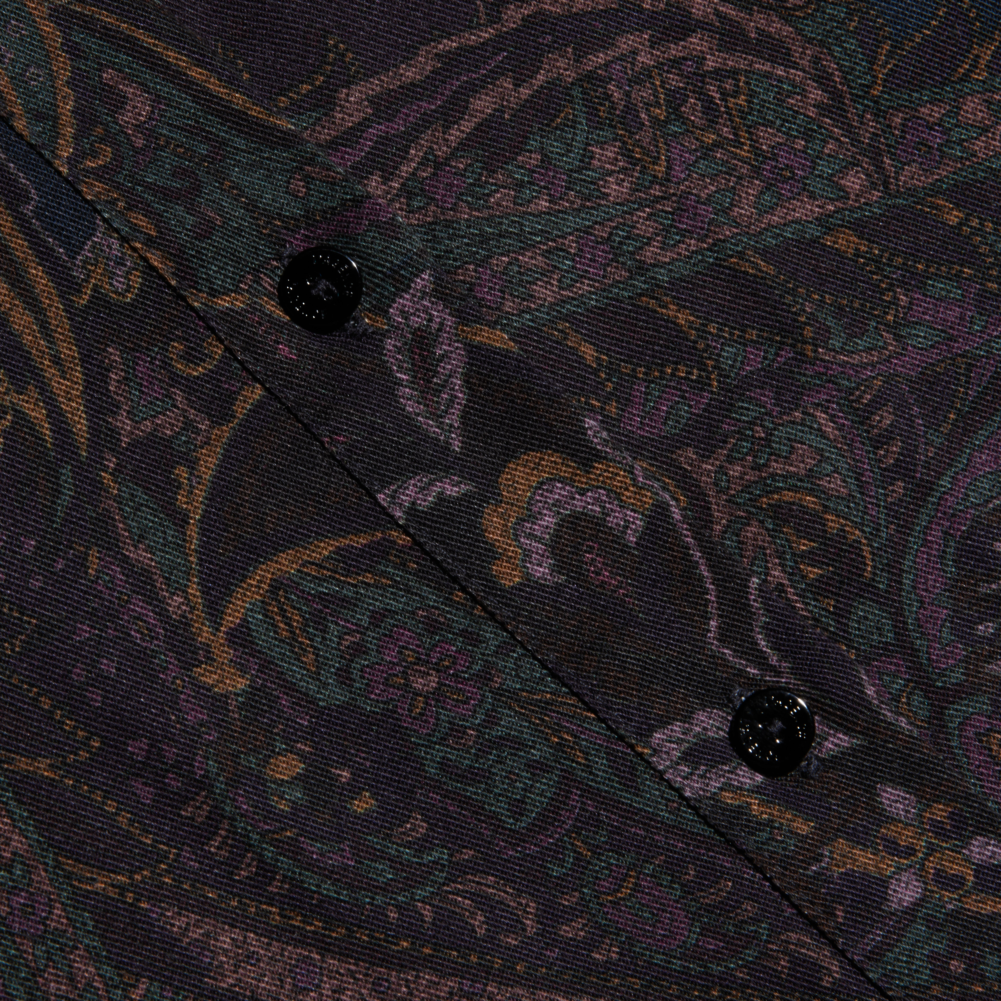 Close-up of the Ellery Button-Down Shirt made from a dark, patterned lightweight twill fabric featuring a muted paisley print and two black buttons sewn along a diagonal seam.