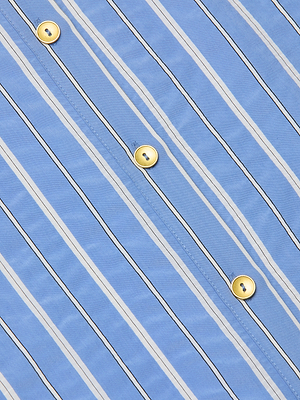 Close-up of the Ellery Poplin Shirt, a blue poplin button-down with white and black vertical stripes, accented by yellow center buttons.