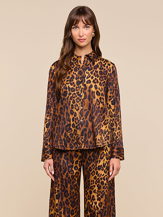 Woman with long brown hair wearing the relaxed fit Ellery Blouse in leopard print, paired with matching pants, standing against a plain beige background and looking directly at the camera with a neutral expression.