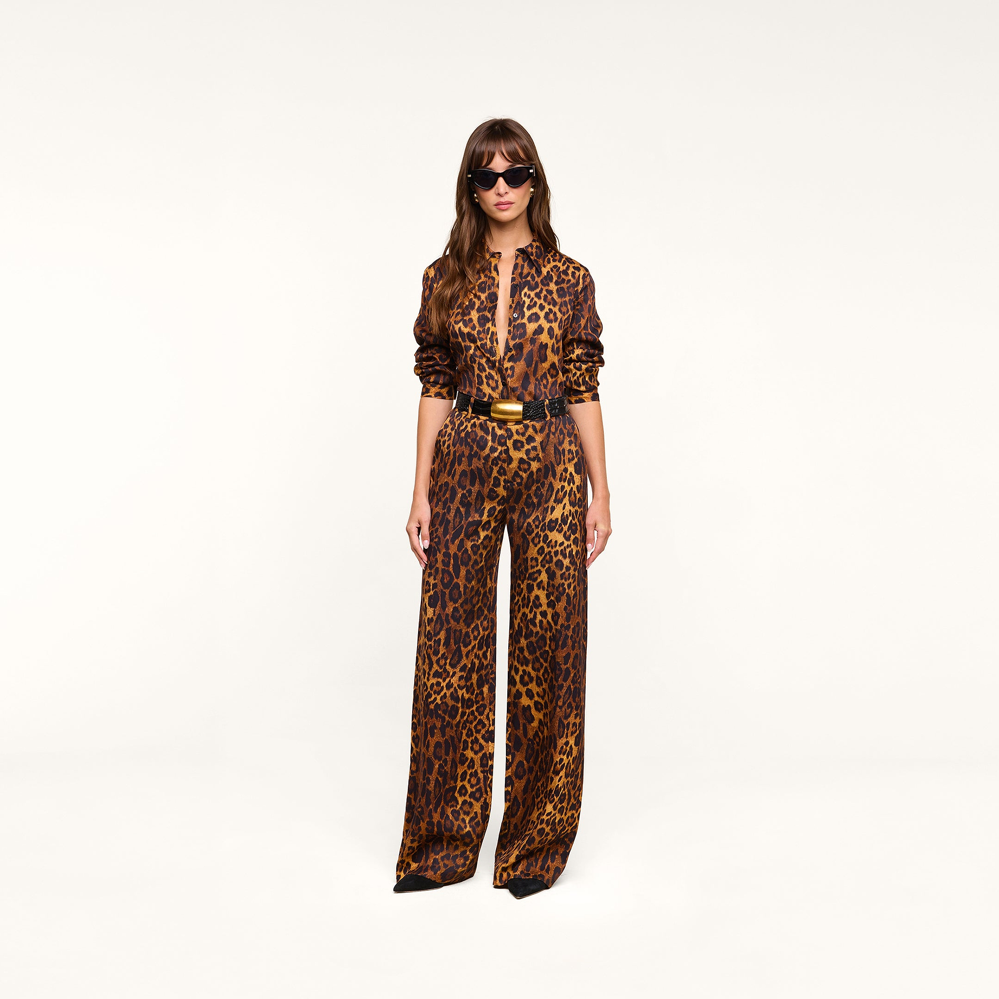 Woman wearing the Ellery Blouse in a relaxed fit leopard print with matching pants, styled with a black belt, black pointed shoes, and sunglasses, standing against a plain white background.