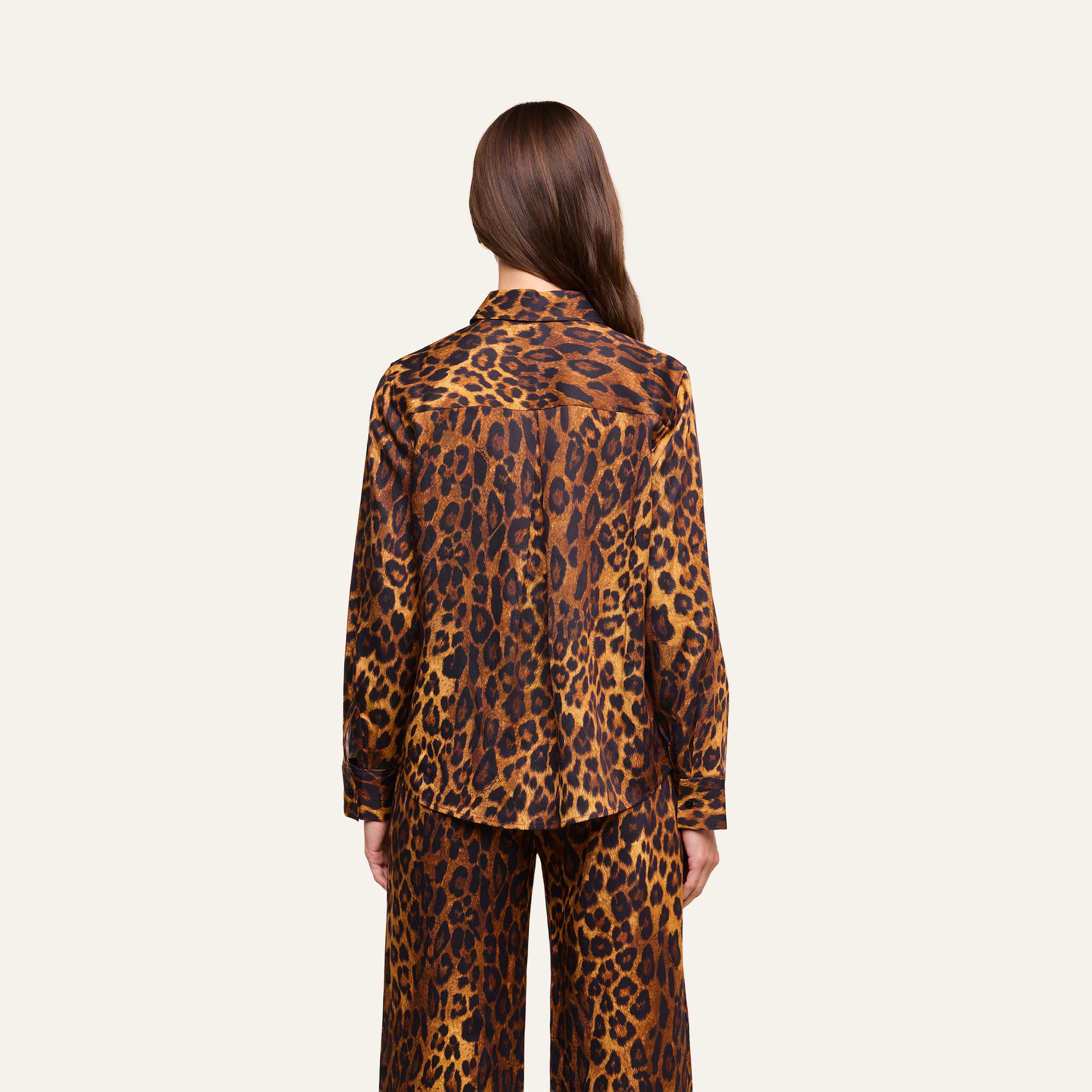 A person with long brown hair is seen from behind, wearing the relaxed fit Ellery Blouse in a leopard print and matching pants set against a plain, light background.