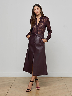 A woman poses against a plain background wearing the Maia Floral Lace Blouse by L'AGENCE in deep burgundy, paired with a matching high-waisted midi leather skirt, black strappy heels, and gold jewelry.
