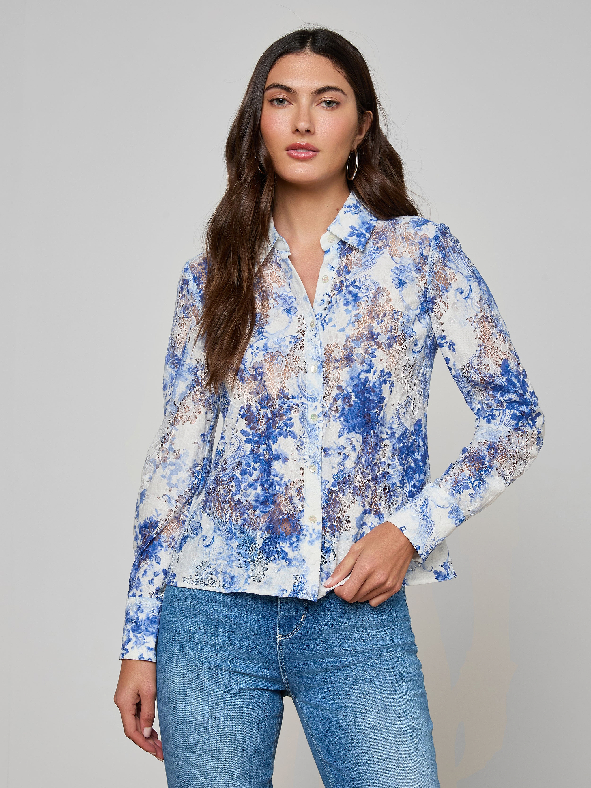 A woman with long brown hair wears the Maia Lace Blouse and light blue jeans, standing against a plain light gray background.