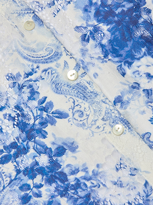 Close-up of the Maia Lace Blouse in navy, showcasing a blue and white paisley pattern and small white buttons along the seam. The intricate lace texture adds refined elegance to this chic button-down blouse.