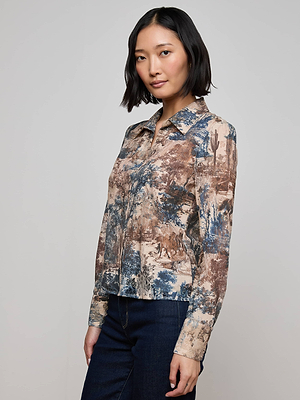A woman with a short bob wears the L'AGENCE Maia Printed Lace Blouse, a collared long-sleeve shirt with a brown and blue Western toile print, posing against a plain light gray background with one hand by her side.
