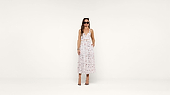 A woman in sunglasses wears a white sleeveless crop top and matching high-waisted, ankle-length skirt with a red and black pattern, standing against a plain white background.