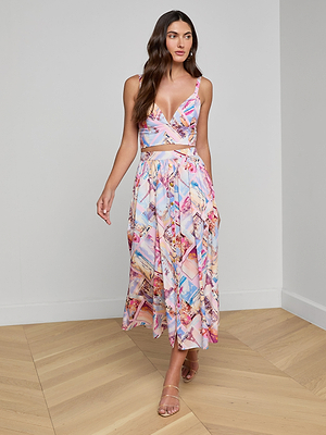 A woman stands indoors on a wooden floor, wearing the Kaori Bralette Top paired with a colorful postcard print flowy midi skirt, and looks slightly to the side.