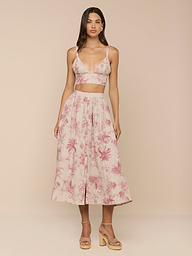 A woman stands in a studio wearing the light pink Kaori Linen Bralette Top in a jungle toile print, paired with a matching midi skirt and tan platform sandals.