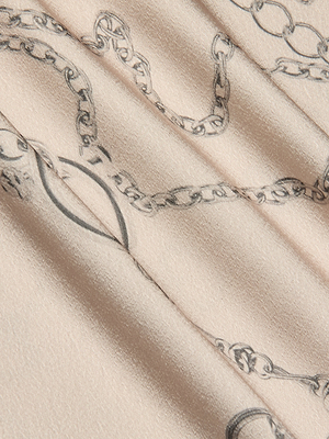 A close-up of beige fabric with a subtle sheen and black horse bit chain print, used to craft the stylish Asami Chain One-Shoulder Blouse.