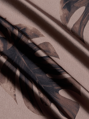 A close-up of beige satin fabric with a dark brown monstera leaf pattern and subtle sheen. Gentle folds add depth—ideal for the Asami Chain One-Shoulder Blouse, creating an elegant, textured look.
