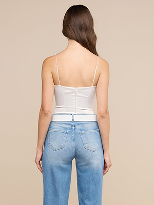 Se ve de espaldas a una mujer con el pelo largo y castaño, que lleva el body «Dara Stretch Satin» con tirantes ajustables y unos vaqueros de cintura alta de color azul claro, sobre un fondo liso de color beige.