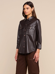 A woman wearing the Avina Leather Shirt in coffee brown, styled with brown pants, stands against a plain light background.