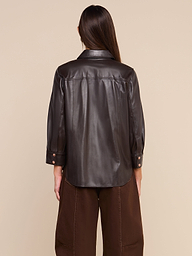 A person with long brown hair stands with their back to the camera against a plain light background, wearing the coffee brown Avina Leather Shirt featuring cuffed sleeves, paired with matching brown pants.