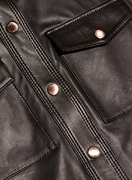 Close-up of the Avina Leather Shirt in lightweight black leather, detailed with shiny copper buttons, visible stitching, two front pockets, and a flap accent.