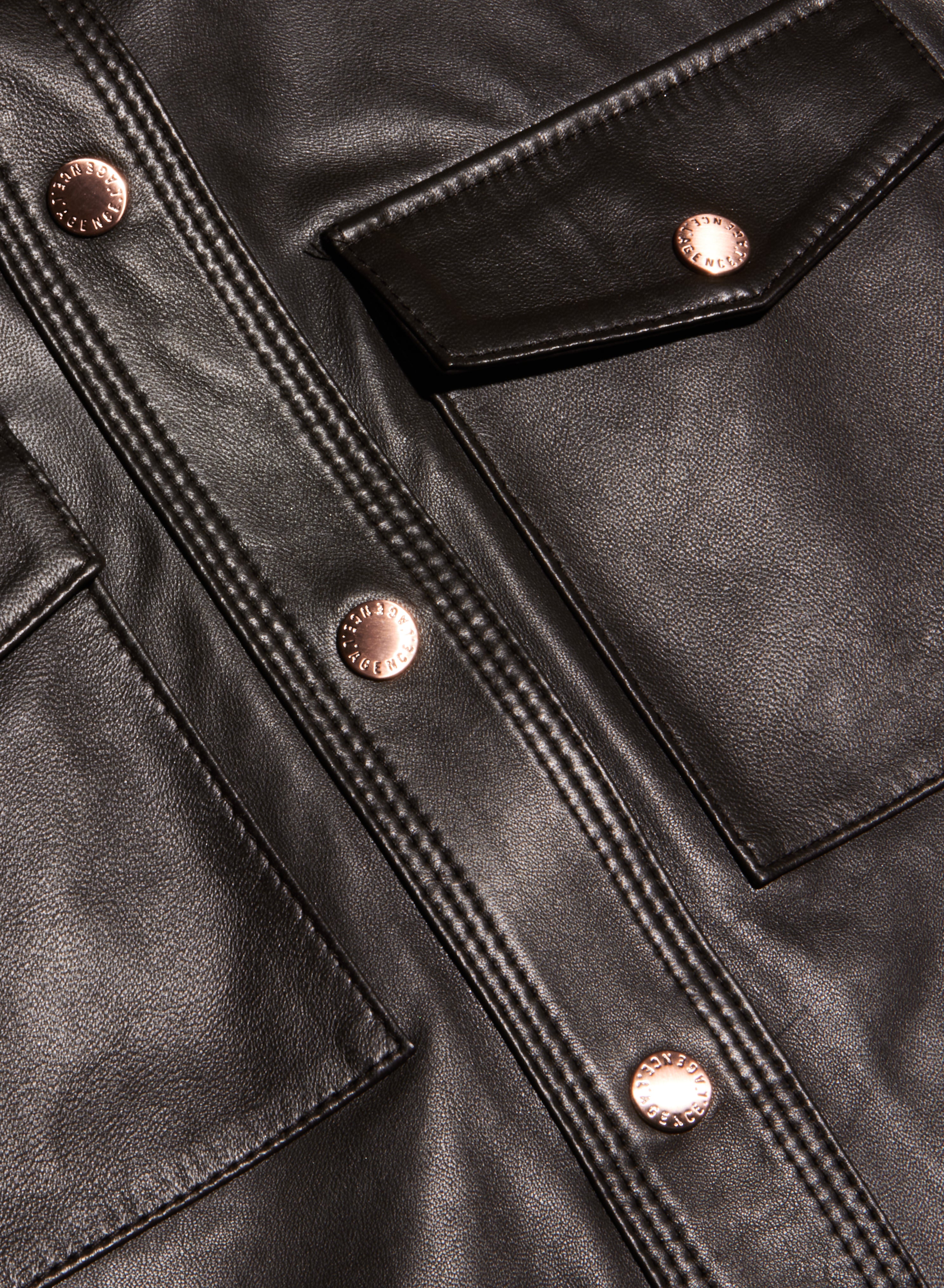 Close-up of the Avina Leather Shirt in lightweight black leather, detailed with shiny copper buttons, visible stitching, two front pockets, and a flap accent.