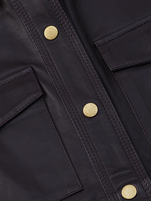 Close-up of the L'AGENCE Avina Leather Shirt in dark brown lambskin, showing two front pockets, three gold snap buttons down the center, visible stitching and texture, and 3/4 length sleeves.