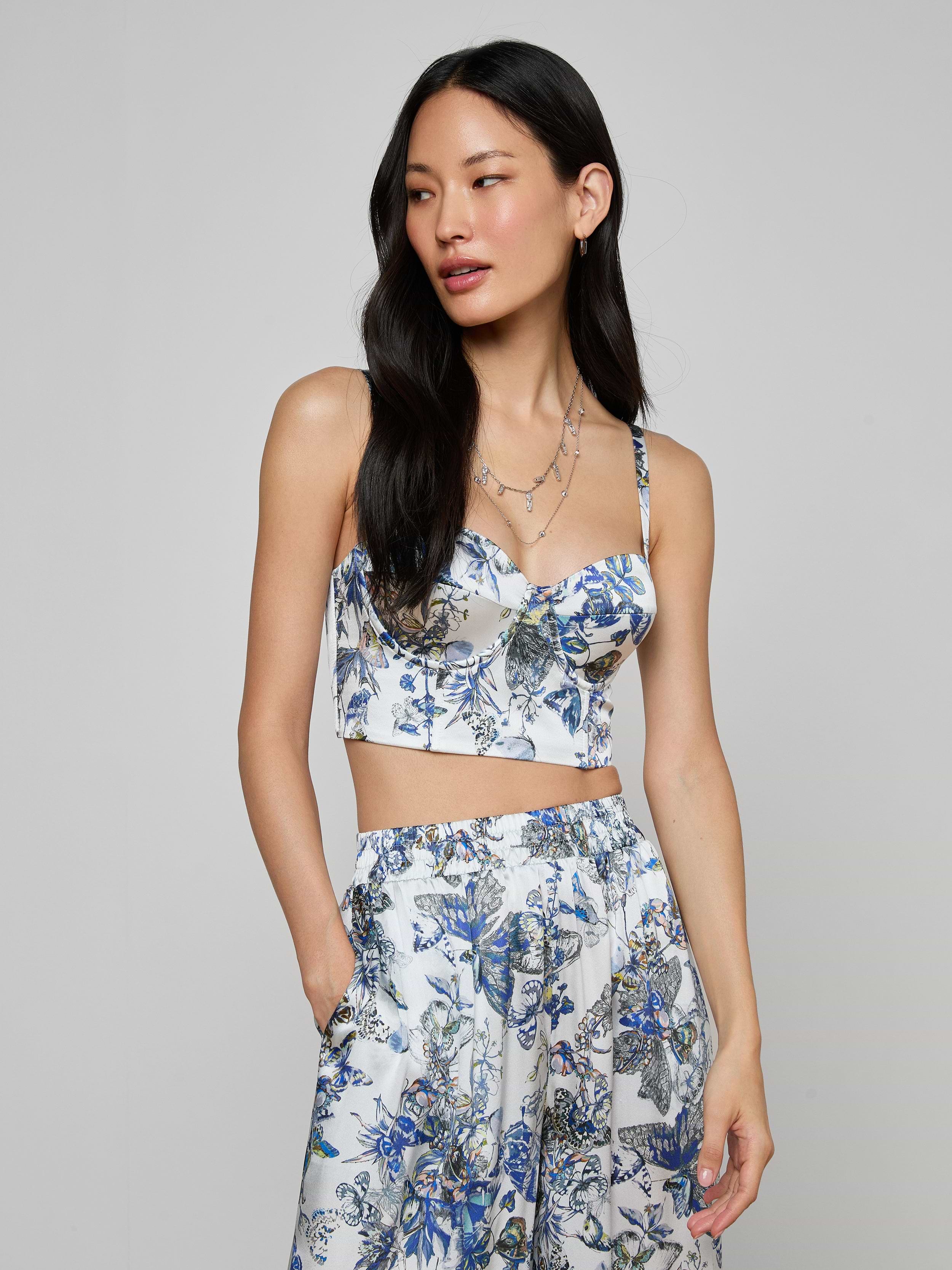 Wearing the Sonya Silk Bustier in blue and white with matching pants, a woman with long dark hair stands against a plain light background, her left hand tucked in her pocket.